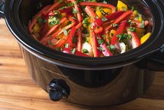 a crock pot filled with vegetables on top of a wooden table