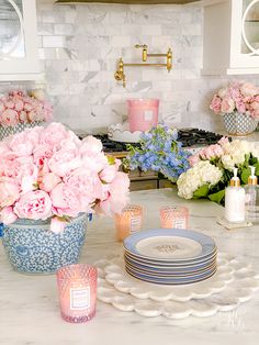 pink and white flowers in blue vases on a kitchen countertop with plates and candles