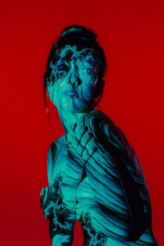 a woman covered in blue and green paint with her face partially obscured by red background