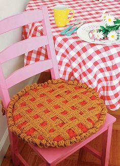 a pink chair with a red and white checkered table cloth on it, next to a yellow plate