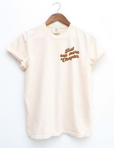 This cute "Just One More Chapter" bookish comfort colors shirt  is the perfect gift idea for readers, book lovers, librarians, literature and literary lovers, and all book nerds. With the rusty orange font colour giving retro vibes, show up to your next book club wearing this aesthetic shirt.  G A R M E N T F E A T U R E S 𝘊𝘰𝘮𝘧𝘰𝘳𝘵 𝘊𝘰𝘭𝘰𝘳𝘴 𝘪𝘯𝘵𝘳𝘰𝘥𝘶𝘤𝘦𝘴 𝘪𝘵𝘴 𝘨𝘢𝘳𝘮𝘦𝘯𝘵-𝘥𝘺𝘦𝘥 𝘶𝘯𝘪𝘴𝘦𝘹 𝘵-𝘴𝘩𝘪𝘳𝘵; 𝘢 𝘧𝘶𝘭𝘭𝘺 𝘤𝘶𝘴𝘵𝘰𝘮𝘪𝘻𝘢𝘣𝘭𝘦 𝘵𝘦𝘦 𝘮𝘢𝘥𝘦 100% 𝘸𝘪𝘵? Bookish Shirt Ideas, Book Graphic Tees, Bookish Tees, Bookish Tshirt, Book Club Shirt Ideas, Bookish Shirts, Book Club Shirt, Bookish Style White T-shirt As Gift, Summer Graphic Print Bookish T-shirt