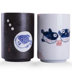 two coffee mugs with fish painted on the cups side by side, one is black and white