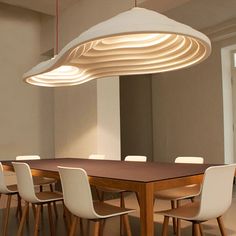 a large wooden table surrounded by white chairs and an oval light fixture hanging from the ceiling