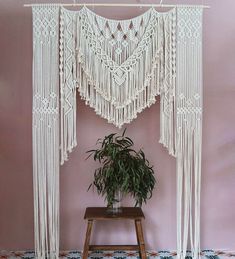 a white macrame hanging from the ceiling next to a potted plant on a stool