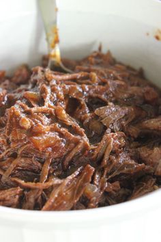 a white bowl filled with shredded beef on top of a table