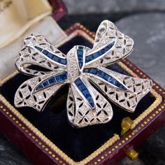 This stunning bow brooch pin features a pierced bow with milgrain details.  The brooch is bead set with forty-five (45) round brilliant cut diamonds, and channel set with thirty-one square and triangle step cut sapphires.  The brooch measures 31.4mm tall by 36.5mm wide by 4.7mm deep.  It is finished with a hinged locking pin back. Luxury Brooches With Single Cut Diamonds, Elegant Brooch With Diamond Accents As Gift, Elegant Diamond Accented Brooch Gift, Luxury Brooches With Single Cut Diamonds As Gift, Elegant Diamond Accents Brooch For Gift, Elegant Diamond Accented Brooches For Gifts, Elegant Diamond Accented Brooches As Gifts, Elegant Brilliant Cut Brooches As Gifts, Elegant Platinum Brooches For Gift