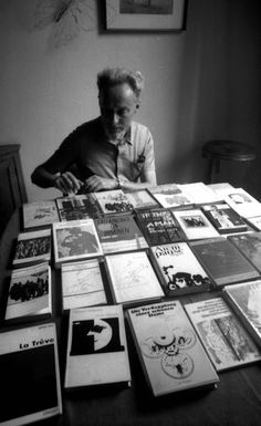 an old man sitting at a table covered with records and cds in black and white