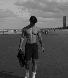 a man with no shirt walking on the beach