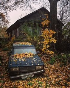 an old car is covered with leaves in front of a wooden house on a fall day