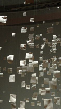 several pieces of paper are suspended from the ceiling in an art installation that is made out of white sheets of paper