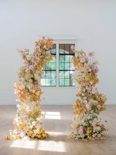 an arch made out of flowers is in the middle of a room with a window