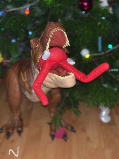 a stuffed dinosaur is in front of a christmas tree with its mouth open and tongue out