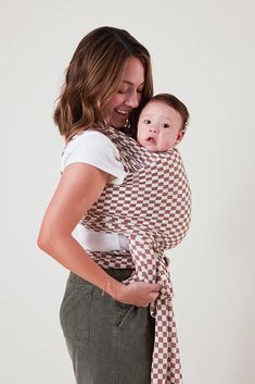 a woman holding a baby wrapped in a brown and white checkered wrap