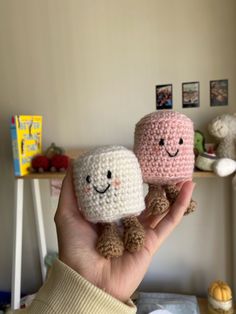 two small crocheted toys are held up in front of a wall with pictures on it