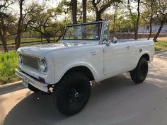 an old white truck parked on the side of the road in front of some trees