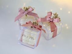 two small clear boxes with pink bows and flowers in them are sitting on a white surface