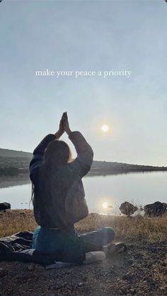 a person sitting on the ground with their hands in the air while looking out over a body of water