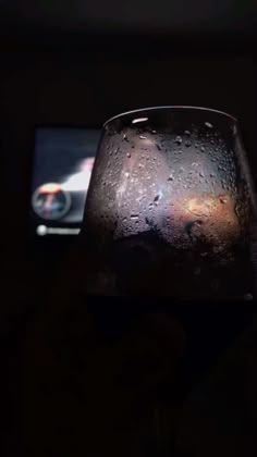 a wine glass with water on it in front of a cell phone and a dark background