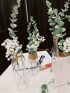 three vases with flowers and greenery are on a table next to a note