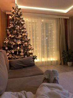 a living room with a christmas tree in the corner and lights shining on the windows