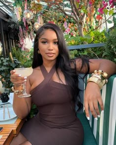 a woman sitting on a chair holding a drink in her hand and looking at the camera