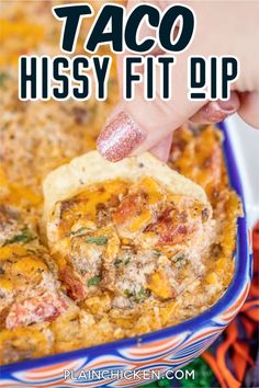 a hand dipping a tortilla chip into a casserole in a blue dish