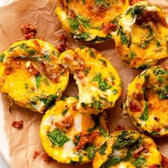 several small muffins on a white plate topped with tomatoes and cheese, garnished with green leaves