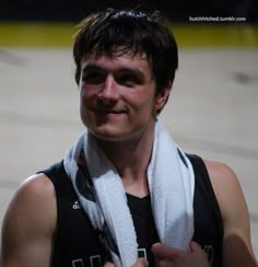 a man with a towel around his neck smiles at the camera while standing on a basketball court