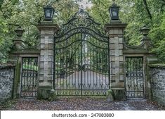 an old iron gate in the middle of a park with stone walls and trees behind it