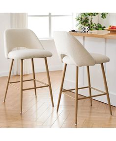 two white bar stools sitting on top of a hard wood floor next to a counter