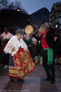 two people dressed in traditional mexican garb dancing on the street at night with other people watching