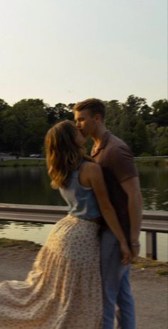 a man and woman are kissing in front of a lake while the sun is setting