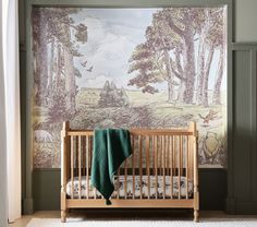 a baby's crib in front of a wall with a forest scene on it