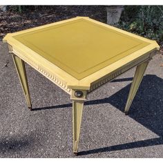 a small yellow table sitting on top of a cement ground next to a planter