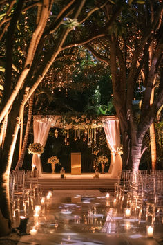 an outdoor wedding setup with candles and flowers on the aisle, surrounded by trees at night