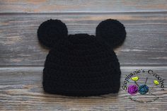 a black crocheted mickey mouse hat on top of a wooden table with the word disney written across it