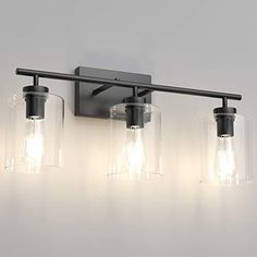 three light bathroom fixture with clear glass shades and black metal frame, on a white wall