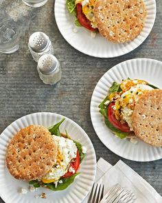 two paper plates with sandwiches on them next to silverware