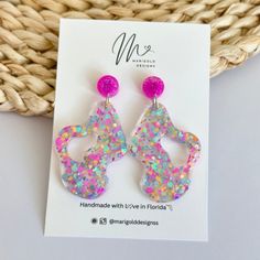 the pink and blue earrings are on display in front of a woven piece of paper