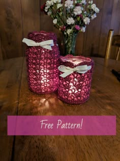 two crocheted jars sitting on top of a wooden table next to a vase with flowers