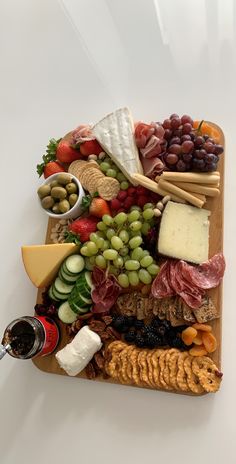 an assortment of cheeses, meats, and fruit on a wooden platter