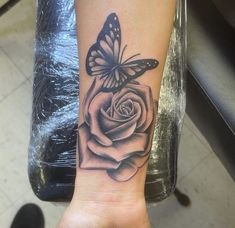 a black and white rose tattoo with a butterfly on it's wrist, in front of a chair