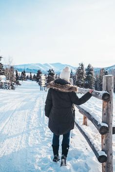 a woman standing on top of a snow covered slope next to a wooden fence and trees