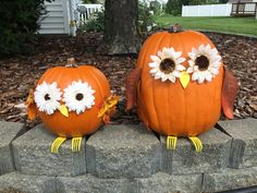 two pumpkins decorated with flowers sitting on top of a stone block in front of a tree