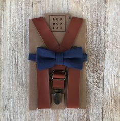 "Cognac brown adjustable faux leather suspenders and navy cotton bow tie set. This set is perfect for your groomsmen, ring bearers, family photos or just because! * \"SET\" includes 1 pre tied bow tie and 1 suspender in selected size. Don't want a set? Want to purchase a neck tie and pocket square? BOW TIES, NECK TIES AND POCKET SQUARES CAN BE PURCHASED INDIVIDUALLY FROM THE LINK BELOW: https://www.etsy.com/LondonJaeApparel/listing/770805020/sage-green-navy-or-terracotta-bow-ties?utm_source=Copy Groomsmen Beach Wedding, Toddler Ring Bearer, Rustic Wedding Groomsmen, Navy Bow Tie, Brown Suspenders, Suspenders Wedding, Leather Suspenders, Suspenders Set, Brown Wedding