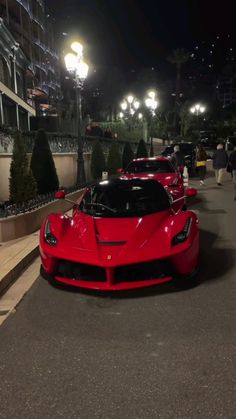 two red sports cars are parked on the side of the road at night in front of some buildings