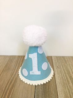 "Please read shop announcement for current processing times and updates. Your birthday boy will look absolutely adorable in this birthday hat for his first birthday or can be customized with any number! Perfect for a party or photo shoot. The hat is available in 2 sizes: Mini (5x4 inches) or full size (7x5 inches). It features light blue felt and a white felt number 1. (Other numbers available upon request) Mini pom pom trim is attached along the base of the hat with a white Pom Pom on top and w Playful Blue Hat For First Birthday, 1st Birthday Hats, Mini Pom, One Banner, Banner Birthday, Blue Party, High Chair Banner, Pom Pom Trim, Birthday Hat