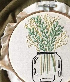 the embroidery is on and it has flowers in a mason jar with green stems inside