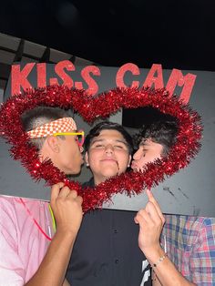 two men standing next to each other in front of a heart shaped sign that says kiss cam