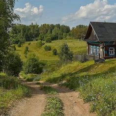 a small house sitting in the middle of a lush green field next to a dirt road